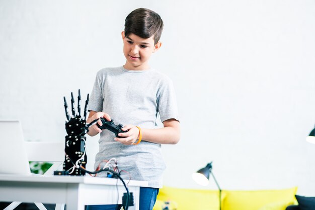 Pleasant smart little boy testing his robotic device by meansof a remote control