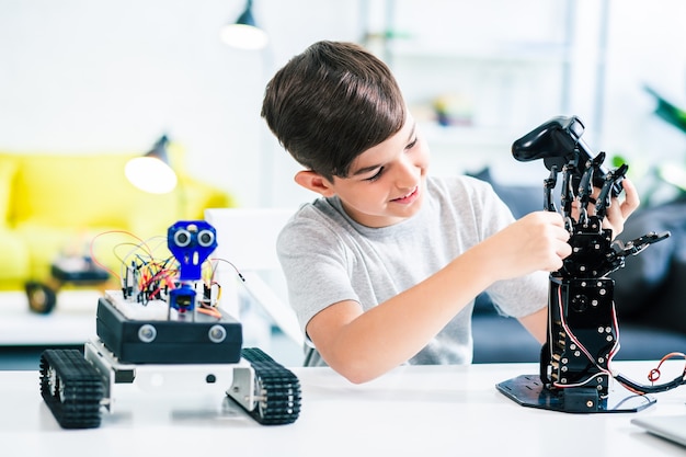 Pleasant smiling schoolboy testing his new robotic device while studying engineering