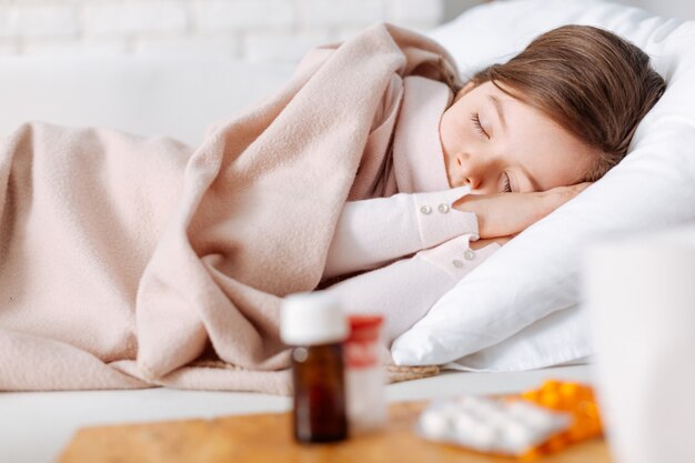 Pleasant tired little girl sleeping and resting at home while suffering from cold