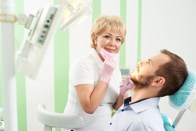 Pleasant woman dentist took off her mask and looks into the camera holding a tool