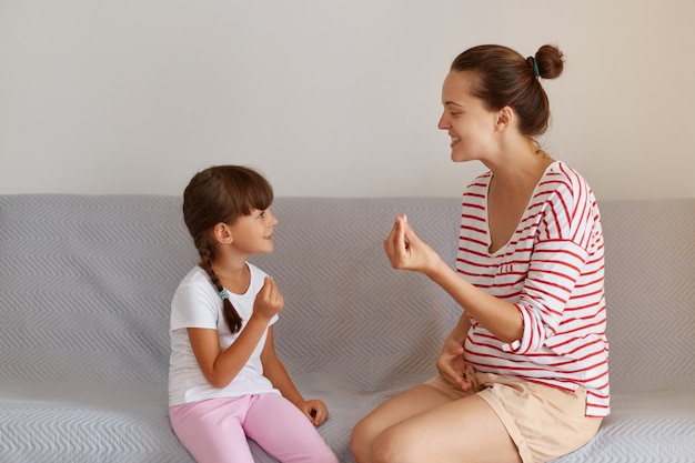 Pleasant young adult speech therapist teaching little female kid right sounds pronunciation, professional physiotherapist working on speech defects or difficulties with small child girl indoors.