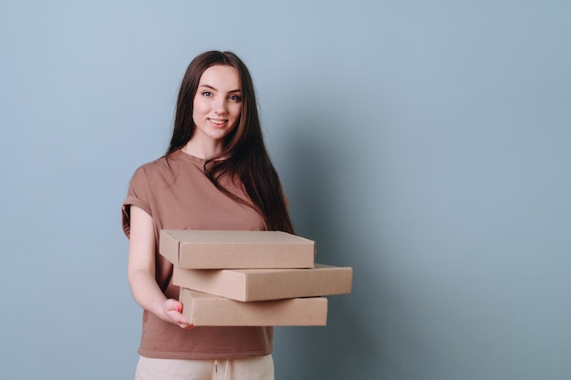 Pleasant young girl holds on outstretched arms a stack of boxes on an empty blue background