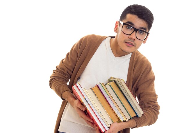 pleasant young man in white tshirt brown cardigan with black glasses holding a pile of books