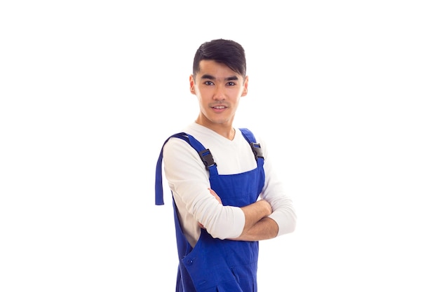 Pleasant young man with dark hair wearing in white shirt and blue overall in studio