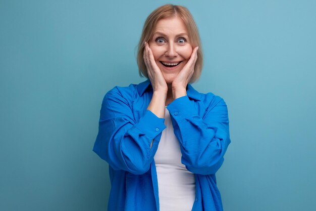 Pleasantly surprised mature woman in casual shirt on blue background