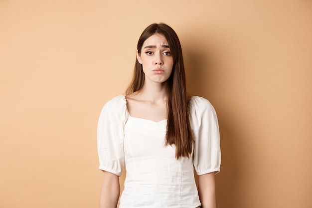 Please I want it. Silly woman make cute sad eyes and begging to buy her something, standing with innocent pleading loo, beige background.