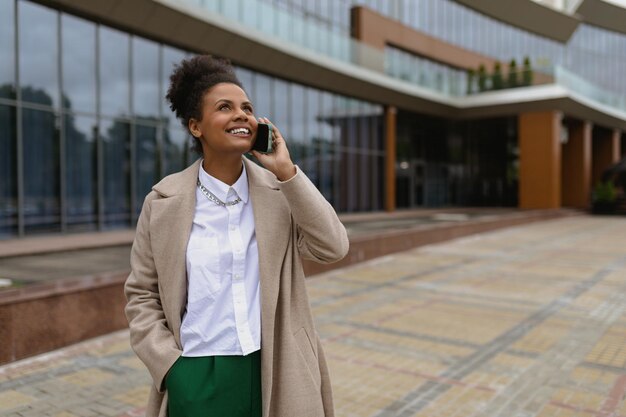 유리 비즈니스 센터를 배경으로 휴대전화로 통화하는 아프리카계 미국인 젊은 여성