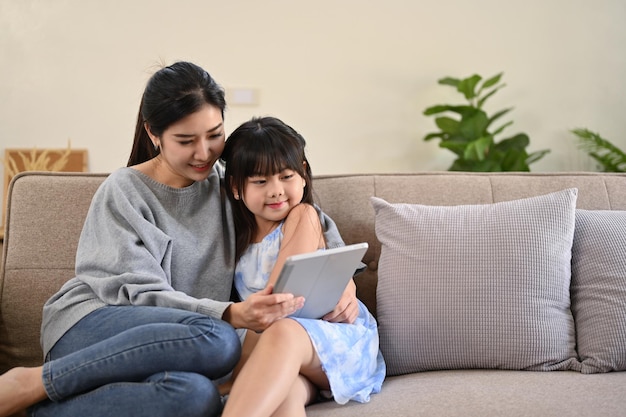 A pleased Asian mom using tablet reading an online fairy tale story to her daughter