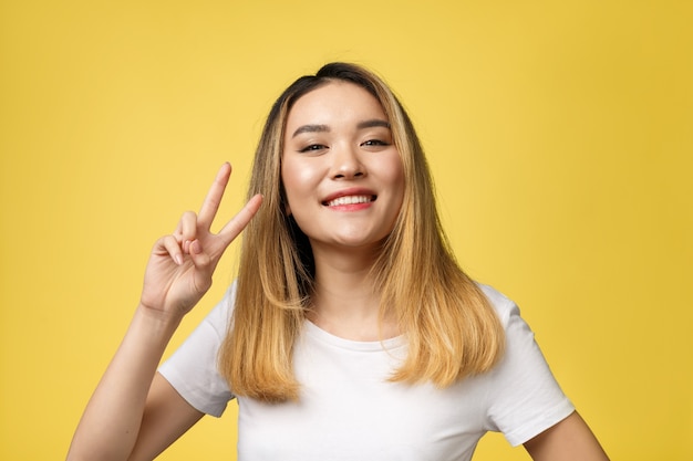 Pleased asian woman in t-shirt showing peace gestures