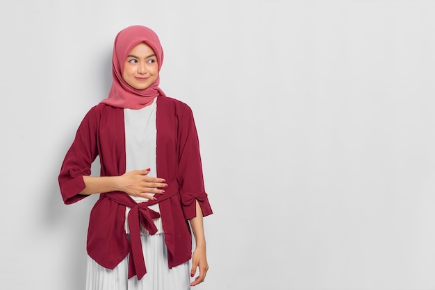 Pleased beautiful asian woman in casual shirt keep hands on the\
stomach and feel satiety after eating tasty isolated over white\
background