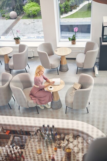 Pleased blonde female person making notes while preparing for meeting, going to drink coffee