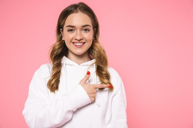 Pleased blonde woman wearing in casual clothes pointing away and looking at the front over pink wall