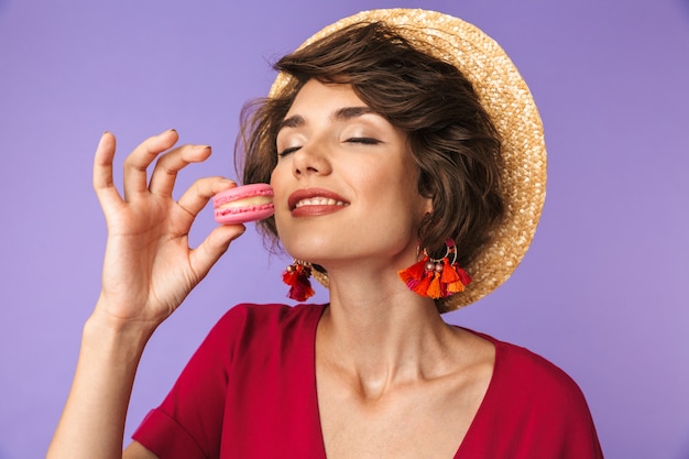 Pleased brunette woman in dress and straw hat eating sweets