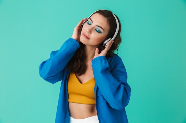 Pleased brunette woman wearing raincoat or jacket listening to music via wireless headphones