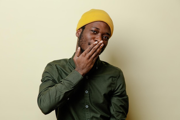 Довольный прикрытый рот рукой молодой африканский американец в шляпе в зеленой рубашке, изолированный на белом фоне