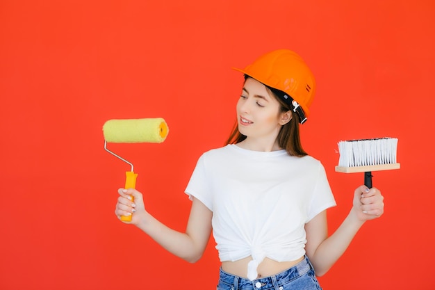 Pleased female holds repairing tools uses paintbrush and roller for decorating room has happy mood