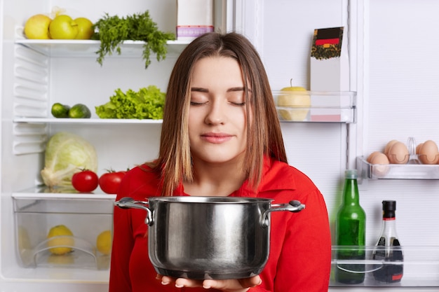 Pleased female holds saucepan