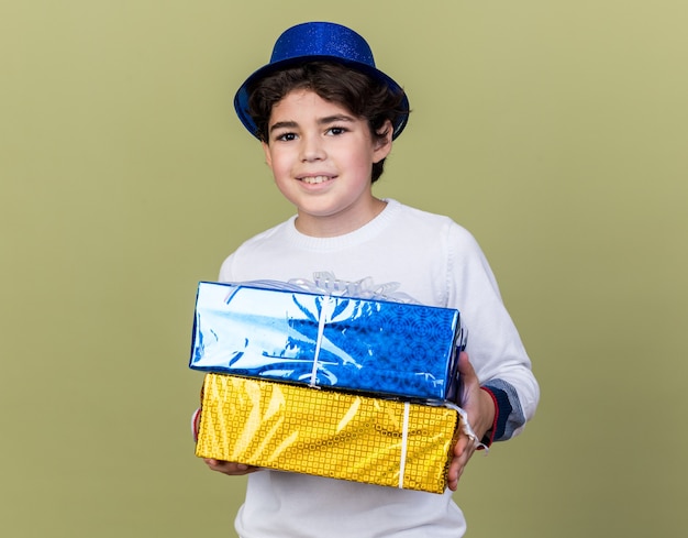 Pleased little boy wearing blue party hat holding gift boxes 