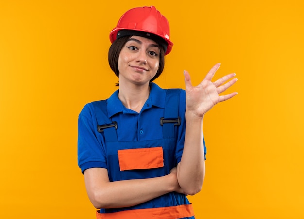 Pleased looking at casmera young builder woman in uniform showing five 