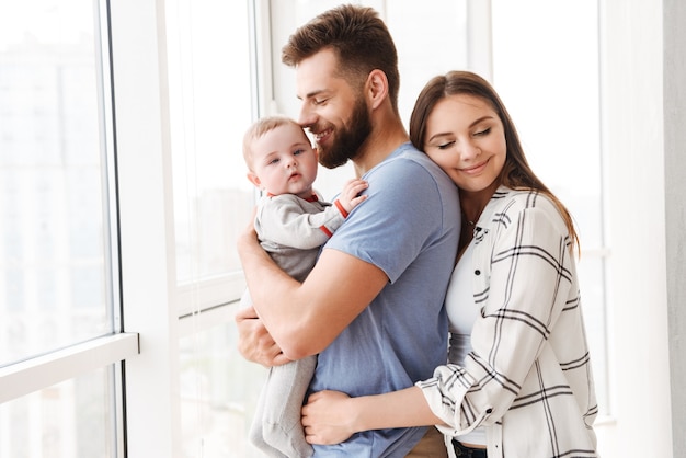 Pleased loving couple parents holding in hands their little son.