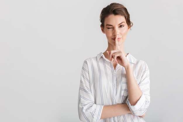 pleased nice woman showing silence gesture and winking isolated on white