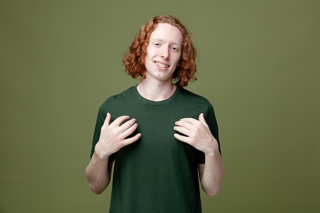 Pleased putting hands on him young handsome guy wearing green t shirt isolated on green background