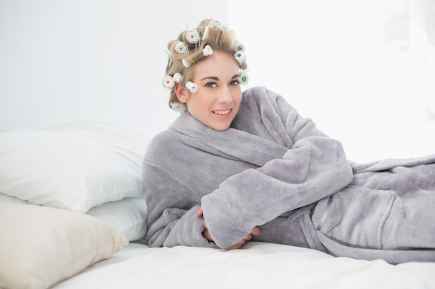 Photo pleased relaxed blonde woman in hair curlers lying on her bed