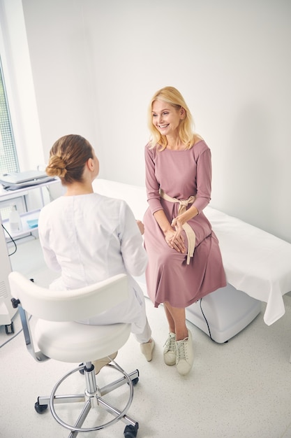 pleased senior woman keeping smile on her face while looking at her practitioner, sitting on the couch