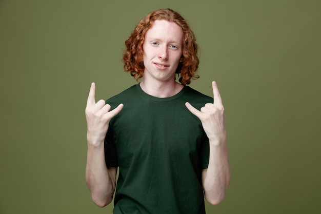 Pleased showing goat gesture young handsome guy wearing green t shirt isolated on green background