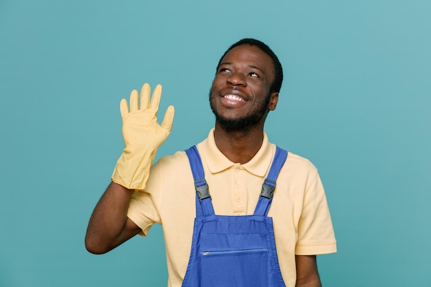 青の背景に手袋をはめた制服を着た若いアフリカ系アメリカ人クリーナー男性のこんにちはジェスチャーを見せて喜んで