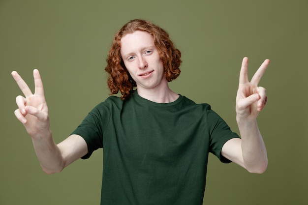 Pleased showing peace gesture young handsome guy wearing green t shirt isolated on green background