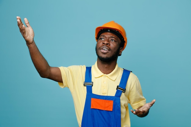 Pleased showing size young african american builder in uniform isolated on blue background