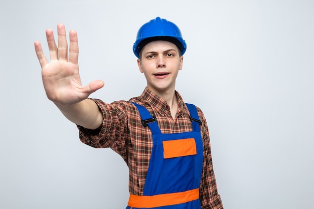 Pleased showing stop gesture young male builder wearing uniform 