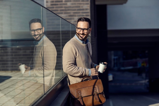 A pleased smart casual man leaning on the glass and drinking a coffee