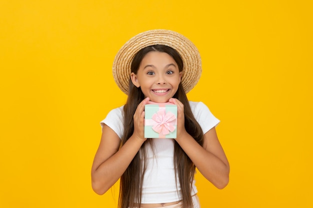 Pleased teen kid hold present box on yellow background