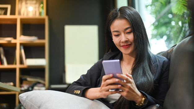 Pleased working woman resting on sofa at her office and using mobile phone