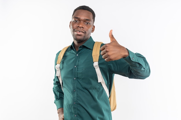 Pleased young afro-american student with backpack thumbing up isolated on white wall with copy space