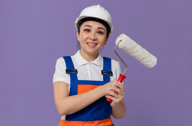 Pleased young asian builder girl with white safety helmet holding paint roller 