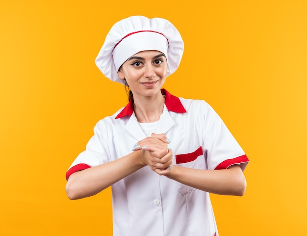 Pleased young beautiful girl in chef uniform showing handshakes gesture isolated on orange wall