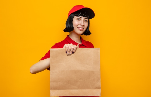 Pleased young caucasian delivery girl holding paper food packaging