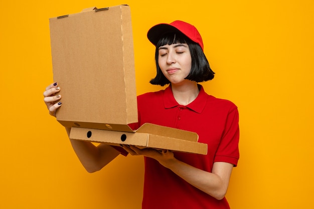 Pleased young caucasian delivery girl holding and sniffing pizza boxes 