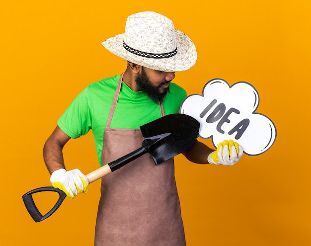 Pleased young gardener afro-american guy wearing gardening hat and gloves holding spade with idea bubble 