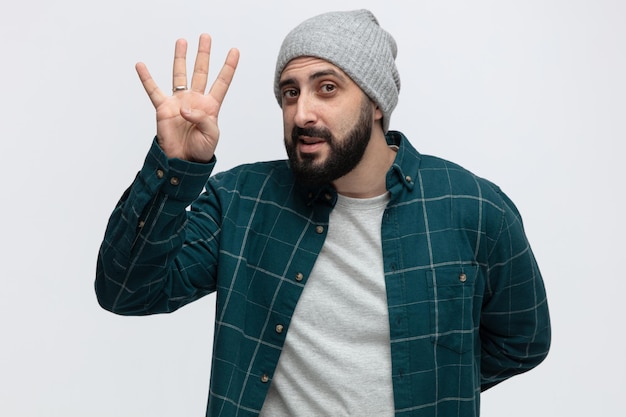 Pleased young man wearing winter hat looking at camera showing four with hand isolated on white background