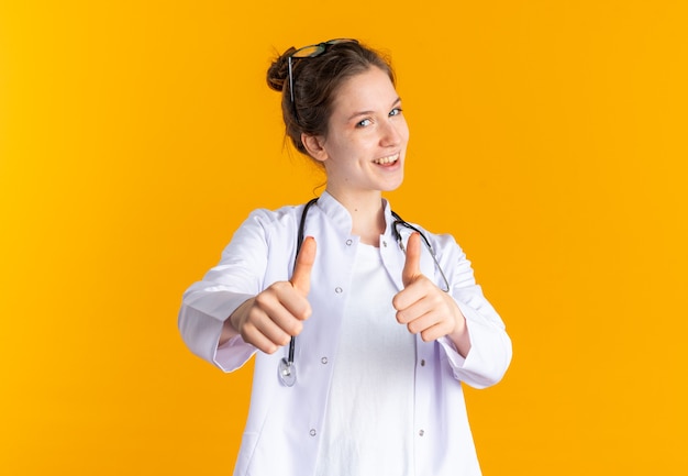 Pleased young woman in doctor uniform with stethoscope thumbing up