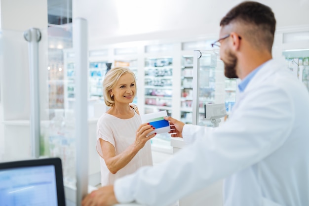 Pleasure communication. Pretty mature female person keeping smile on her face while taking package with pills