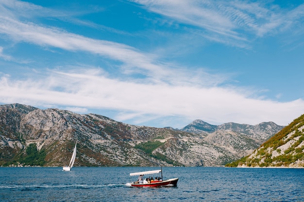 A pleasure red motor boat with an awning from the sun sails with people off the coast of the city