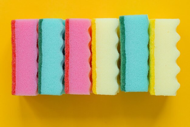 Plenty of bright multicolored sponges on yellow background top view Cleaning concept