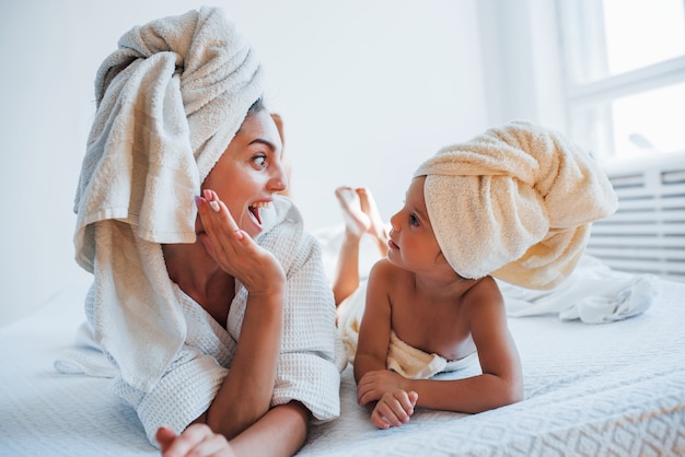 Plezier hebben. Jonge moeder met haar dochter heeft schoonheidsdag binnenshuis in witte kamer.