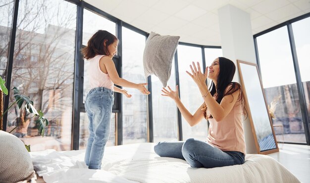 Plezier hebben met kussen op bed Jonge moeder met haar dochter die weekend samen op kamer doorbrengt