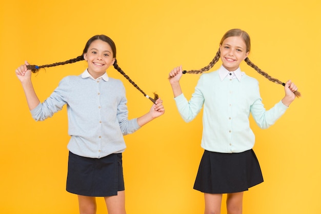 Plezier hebben samen slimme kleine meisjes op gele achtergrond kid mode vriendschap en zusterschap kennis dag gelukkige jeugd gelukkige meisjes in schooluniform onderwijs concept terug naar school